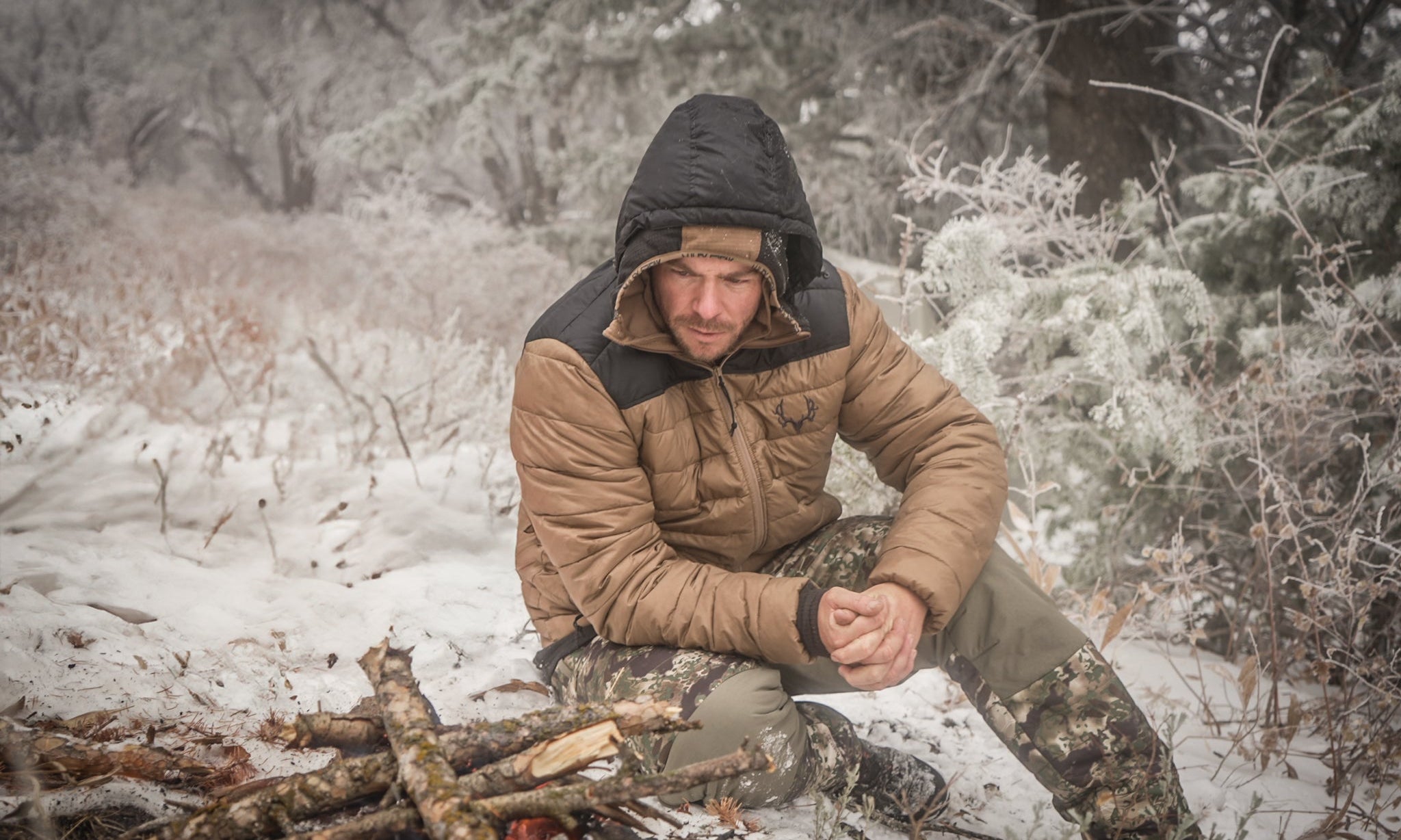 A hunter sitting by a fire in the snow in the high country