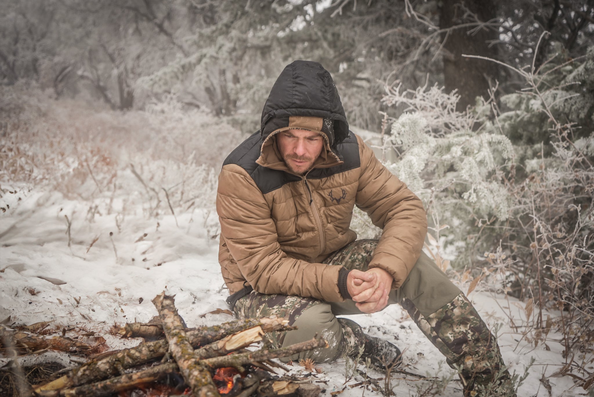 A hunter sitting by a fire in the snow in the high country